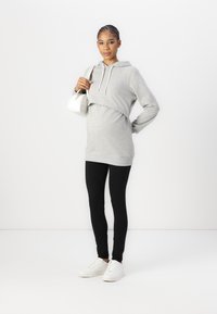 Sweater cropped cinza com cordões, combinado com leggings pretas e ténis brancos. O conjunto tem um ajuste descontraído e materiais macios.