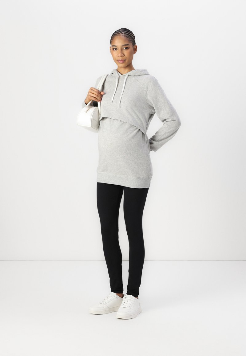 Sweater cropped cinza com cordões, combinado com leggings pretas e ténis brancos. O conjunto tem um ajuste descontraído e materiais macios.