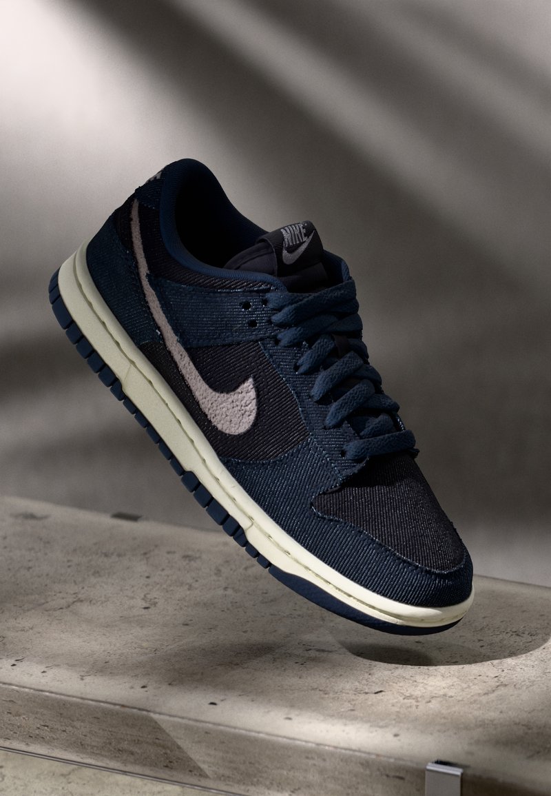 Baskets Nike bleu foncé avec semelle blanche et logo swoosh, lacets attachés, exposées sur une surface en béton avec une ombre douce en arrière-plan.
