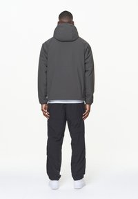 Mörkgrå vadderad jacka med hög krage och långa ärmar, i kombination med svarta cargobyxor och vita sneakers, sedd bakifrån.