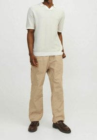 Bílý pletený polokošile s krátkým rukávem a véčkovým výstřihem, v kombinaci s béžovými volnými kalhotami a tmavě hnědými šněrovacími botami.