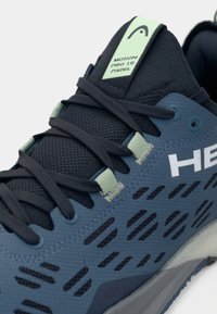 Niebieski but sportowy z teksturowaną siateczkową cholewką, kontrastującymi granatowymi sznurowadłami oraz jasnozieloną metką. Posiada wzorzystą wentylację boczną i gumową podeszwę.