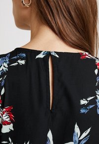 Black fabric top with a floral print in red, white, and blue. Features a keyhole back detail and smooth texture.