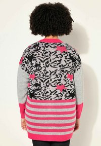 Suéter de punto con un cuerpo gris, patrón abstracto en negro y rosa, acentos en rosa y dobladillo a rayas. Mangas largas y diseño de corte relajado.