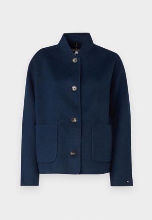 Marineblaues Wollmischgewebe-Jacket mit Stehkragen, frontaler Knopfverschluss, zwei aufgesetzten Taschen und dezenter Logo-Akzentuierung am Ärmel.
