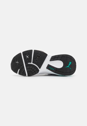 Semelle d'une chaussure de sport avec une bande de roulement noire et blanche, présentant des motifs en zigzag, logo Puma et étiquette "PUMAGRIP" sur fond blanc.