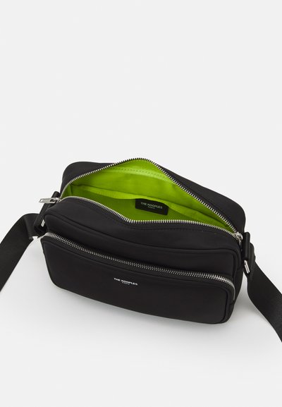 Melnā sintētiskā crossbody soma ar divām rāvējslēdzēju nodalījumiem un dzīvīgu zaļu iekšpusi. Iekļauj sudraba detaļas un regulējamu siksnu.