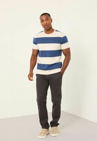 Striped short-sleeve t-shirt in navy and cream, paired with dark gray pants and light beige sneakers, standing against a neutral background.