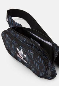 Black and blue patterned waist bag with zipper closure, striped adjustable strap, and white Adidas logo on the front. Compact design.
