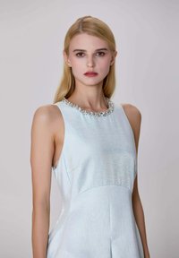 Robe sans manches bleu clair avec un tissu texturé, une silhouette ajustée et un détail décoratif au col orné de gemmes.