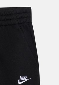 Pantaloni da tuta neri Nike con cintura elastica, tasca laterale e logo Nike ricamato bianco vicino alla tasca.