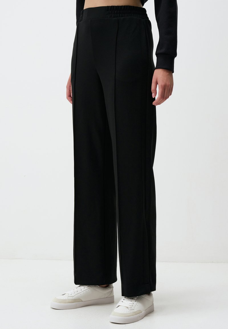 Czarne spodnie o szerokich nogawkach z elastycznym paskiem, wykonane z gładkiego materiału; w połączeniu z białymi sneakersami z delikatnymi akcentami.