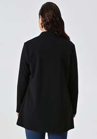 Schwarze Jacke mit langen Ärmeln und rundem Kragen, aus weichem Material gefertigt. Bietet eine ausgestellt geschnittene Silhouette und eine glatte Textur.