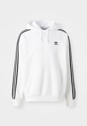 Bijela majica s kapuljačom koja ima prednju džepnu torbu, vezicu za kapuljaču i crni Adidas logo. Ima crne pruge duž rukava. Mekana tekstura tkanine.