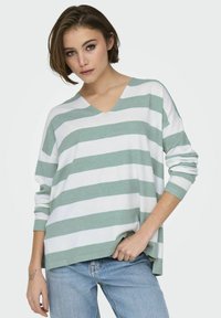 Pull léger à col en V avec des rayures horizontales vertes et blanches alternées, manches longues et coupe ample. Matière en tricot texturé.