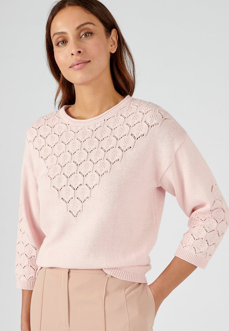 Pull léger rose avec un motif en dentelle sur les épaules et le haut de la poitrine, doté d'un col rond et de manches trois-quart.