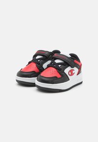 Černé a červené tenisky s bílou podrážkou, vybavené polstrovaným černým jazykem, síťovanými detaily, perforacemi a nastavitelným zapínáním na pásek.