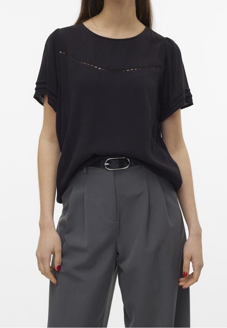 Un blouson noir à manches courtes avec une bande texturée sur la poitrine, associé à un pantalon gris taille haute avec des plis et une ceinture.