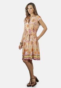 Vestido de manga corta, estampado en naranja, rosa y blanco, con cinturilla ajustada y falda hasta la rodilla. Incluye un diseño de botones en la parte delantera y una abertura lateral.