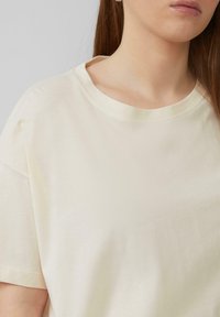 Crème kleurige katoenen t-shirt met een ronde halslijn en korte mouwen. Zachte textuur en een relaxte pasvorm, zichtbare stiksels op de kraag.
