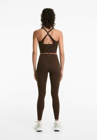 Brown athletic crop top with crisscross back straps paired with matching brown leggings. Smooth texture with logo detailing on waistband.