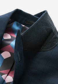 Marineblazer met een geweven buitenstof en een contrasterende vilten kraag. Binnenvoering heeft een geometrisch patroon in blauw, roze en zwart.