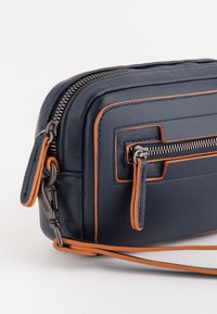 Bolso cruzado de cuero azul marino con detalles en naranja, bolsillo frontal con cremallera y correa desmontable sobre fondo blanco.