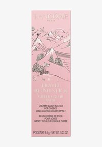 Emballage rose pour le Lancôme Travel Blush Stick, présentant des graphiques de montagnes et des accents argentés. Le texte met en avant une formule crémeuse et la commodité de voyage.