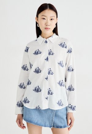 White button-up shirt with navy floral print, long sleeves, pointed collar, and soft texture, paired with a denim mini skirt.