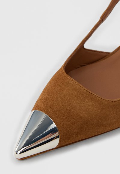 Chaussure en daim marron avec un bout pointu et un accent argenté métallique à l'extrémité. Présente un design élégant avec un côté ouvert et une texture douce.