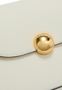 Clutch in pelle bianca testurizzata con chiusura a forma rotonda dorata, dotato di branding embossato e cuciture nere a contrasto lungo i bordi.