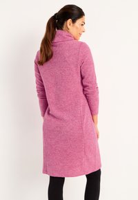 Fittad klänning med långa ärmar i en texturerad rosa stickning med hög krage, som når till mitten av låret. Har slitsar på sidorna och rak skärning.