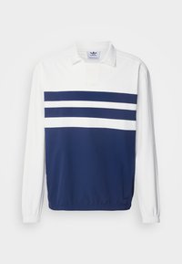 Balts un tumši zilas Adidas regbija krekls garām piedurknēm ar divām horizontālām baltām svītrām pāri tumši zilajai krūtīm un elastīgām piedurknēm.