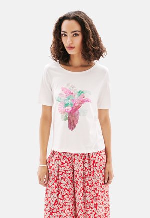 T-shirt blanc avec un graphique coloré représentant un oiseau et des feuilles tropicales. Col rond, manches courtes. Assorti à un pantalon large à imprimé floral rouge.