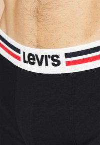 Fekete boxer alsónadrág fehér elasztikus derékpánttal, amelyen piros és kék csíkok láthatók. A derékpánton a "Levi's" logó fekete betűkkel szerepel.