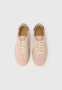 Zapatillas de ante rosa claro con franjas crema, cordones beige y parche marrón en el talón. Cuenta con una punta redondeada y suela de goma texturizada.