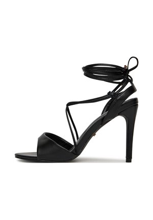 Czarna sandałka na wysokim obcasie z odkrytymi palcami, cienkimi paskami krzyżującymi stopę oraz wiązaniami wokół kostki.