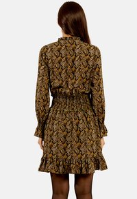 Abito a maniche lunghe con vita arricciata e orlo a volant. Presenta un tessuto marrone scuro con una stampa paisley in tonalità oro e crema.