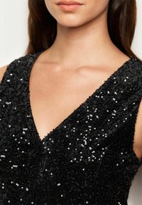 Czarna sukienka ozdobiona cekinami z głębokim dekoltem w kształcie litery V i teksturowanym materiałem, charakteryzująca się skomplikowanym wzorem błyszczących materiałów.