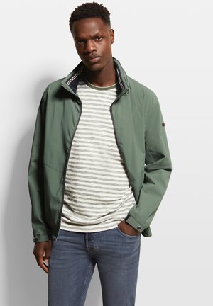 Green lightweight jacket with a high collar, zip front, and a smooth finish, worn over a striped shirt. Paired with blue jeans.