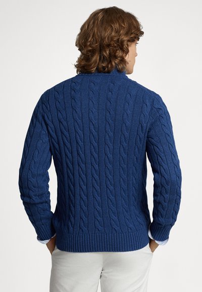 Πλεκτό πουλόβερ σε ναυτικό μπλε, με ριμπ τελείωμα και μανσέτες, διαθέτει ανάγλυφο σχέδιο και ψηλό γιακά. Η πίσω όψη παρουσιάζει περίπλοκη πλέξη.