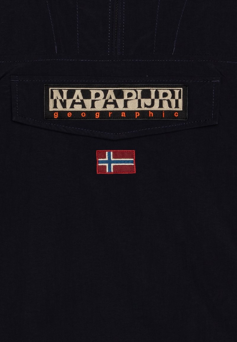 Tessuto blu navy con un'etichetta ricamata prominente "NAPAPIJRI geographic" e una piccola bandiera norvegese. Le cuciture ravvicinate mettono in risalto i dettagli.