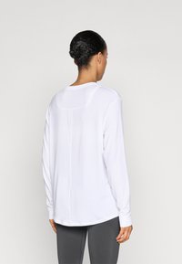 Λευκό μπλουζάκι με μακριά μανίκια και στρογγυλή λαιμόκοψη, με διακριτική ραφή στο πίσω μέρος και απαλή υφή υφάσματος, συνδυασμένο με γκρι κολάν.