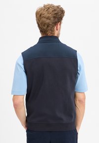 Marineblauwe mouwloze vest met een zachte textuur en lichte padding, voorzien van een hoge kraag en een contrasterende blauwe mouwonderlaag.
