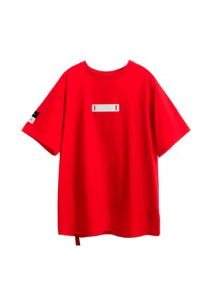 Camiseta de algodón roja, dise�ño oversized, mangas cortas, con una etiqueta rectangular blanca en el frente y un detalle de bucle en el lateral.