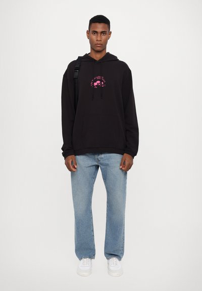 Black hooded sweatshirt with pink graphic print, front pouch pocket, paired with light blue straight-leg jeans and white sneakers.