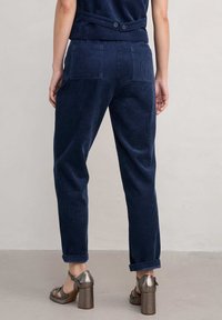 Mornarske kordne hlače z sproščenim krojem, ki vključujejo dve zadnji žep in zavihke na hlačnicah. V kombinaciji z sandali z blok peto v metalik barvi.