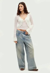 White crochet cardigan over a fitted white top, paired with loose-fitting light blue jeans. The jeans have a faded texture and slight distressing.