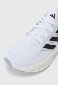 Scarpa sportiva bianca con tomaia in maglia testurizzata e dettagli neri. Presenta lacci piatti e una suola ammortizzata con il marchio "LIGHTBOOST".
