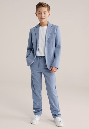 Costume bleu clair avec une veste ajustée et un pantalon à taille élastique, combinés avec un t-shirt blanc et des baskets blanches. Texture lisse.